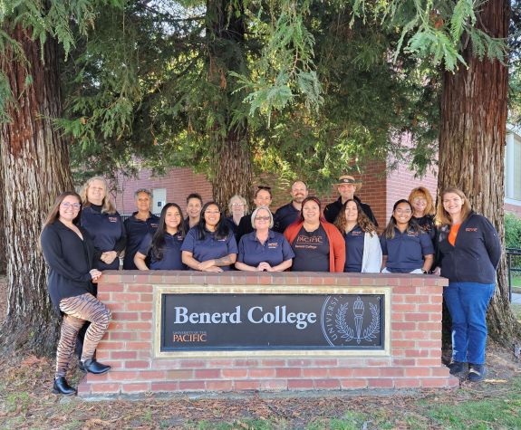 The staff of Benerd College standing behind the Benerd sign